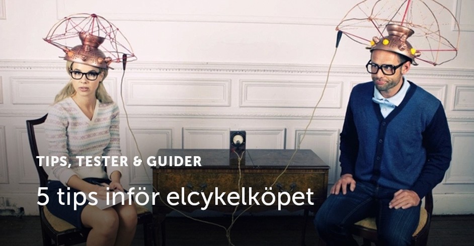 En man och kvinna sitter på varsin stol vid ett bord, med konstiga saker på huvudet som ska föreställa att de blir testade.